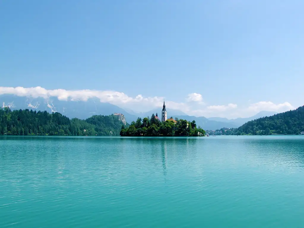 Lago alpino con una isla en el centro coronada por una iglesia y un castillo medieval sobre un acantilado, la imagen más icónica del país.